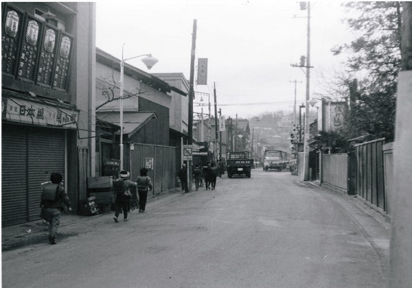 大山街道を中心に据えた写真。道の両側には商店の看板が見え、街道にはランドセルを背負った子どもたち歩いている。